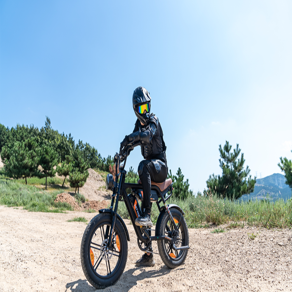 Person riding a black electric bike on a dirt path with a clear blue sky and greenery in the background.