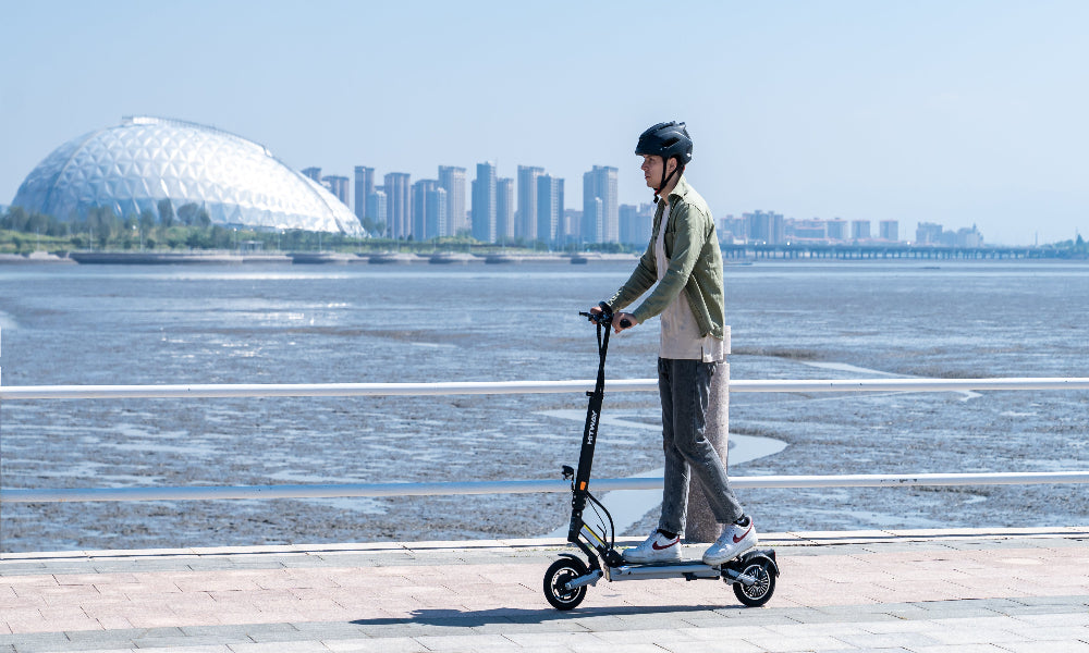 Person riding an electric scooter on a path with a cityscape in the background