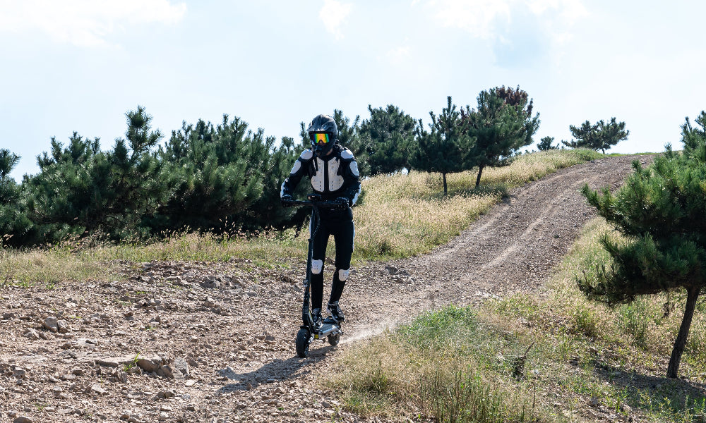 Person in motorcycle gear standing on a dirt path with trees in the background
