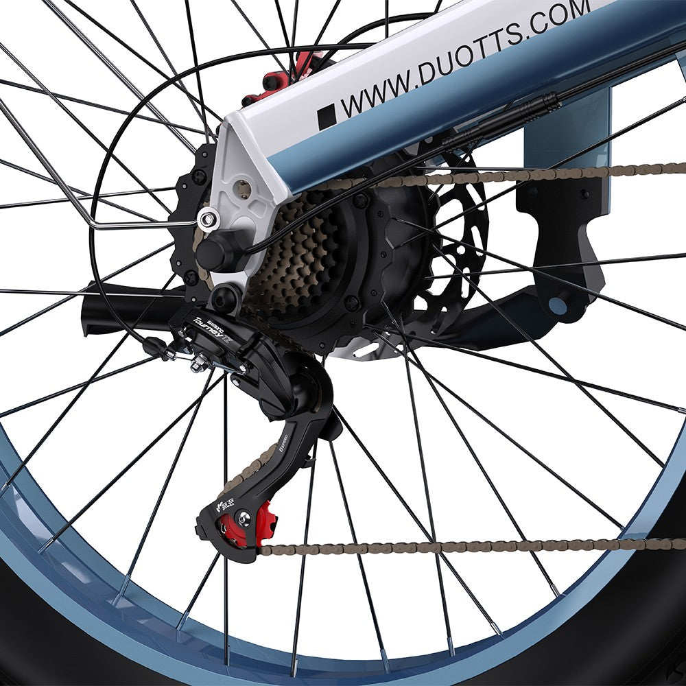 Close-up of a bicycle wheel with gear and chain mechanism, featuring Duotts.com branding.