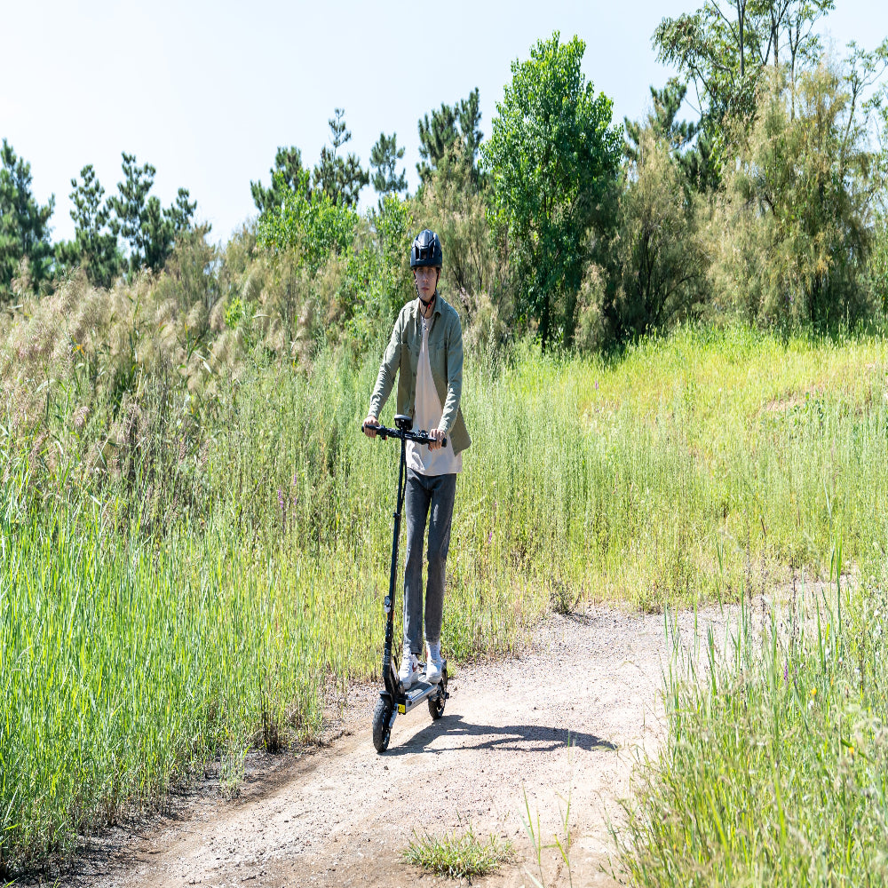 Person riding a scooter on a dirt path with greenery in the background
