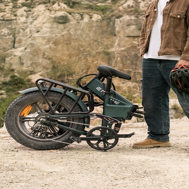 Person standing next to a folded electric bike in a rocky outdoor setting