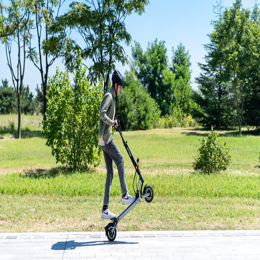Person riding an electric scooter on a path with greenery in the background