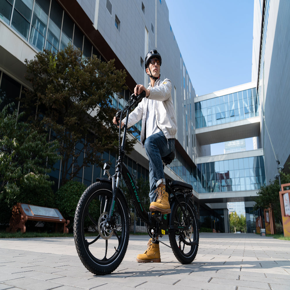 Person sitting on an electric bike in an urban setting with modern buildings.