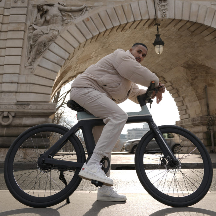 Man riding a black bicycle in an urban setting with stone arches in the background