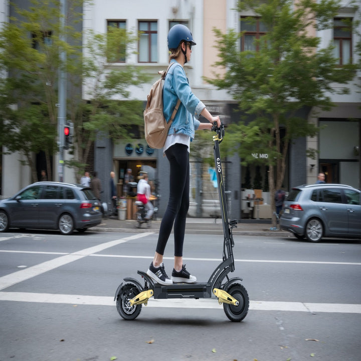 Person riding an electric scooter on a city street with buildings and cars in the background