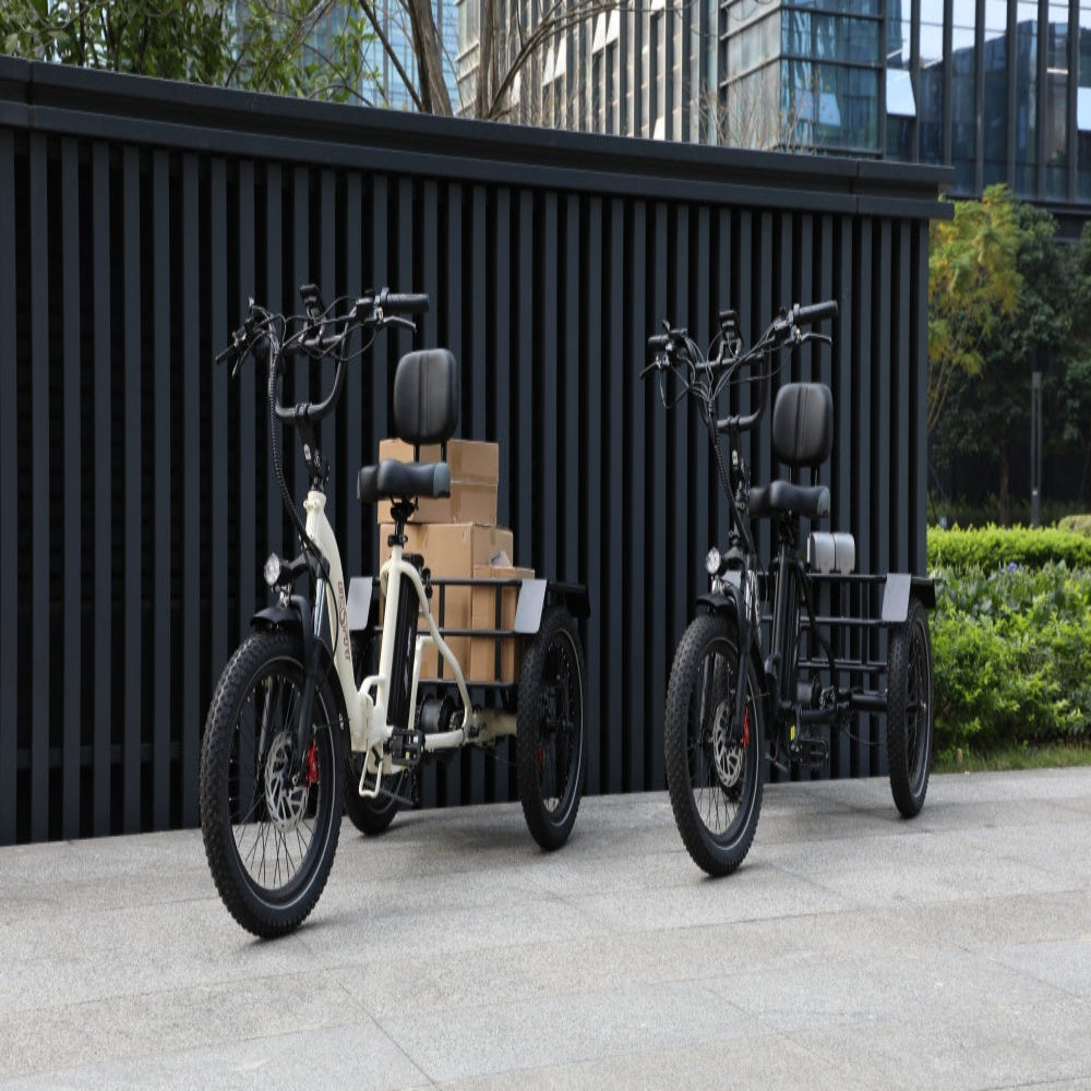 Two electric tricycles with cargo trailers parked against a black wall.