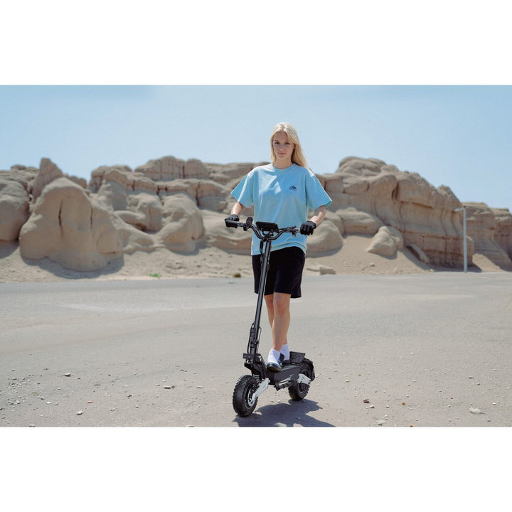 Person riding an electric scooter in a desert-like setting with rocky formations.