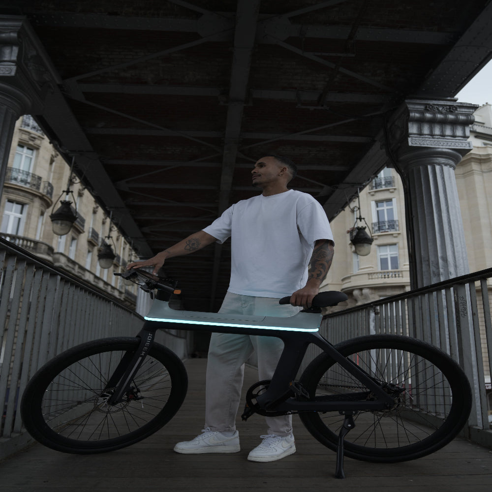 Person holding a laptop on a reflective surface with a bicycle nearby, urban setting.