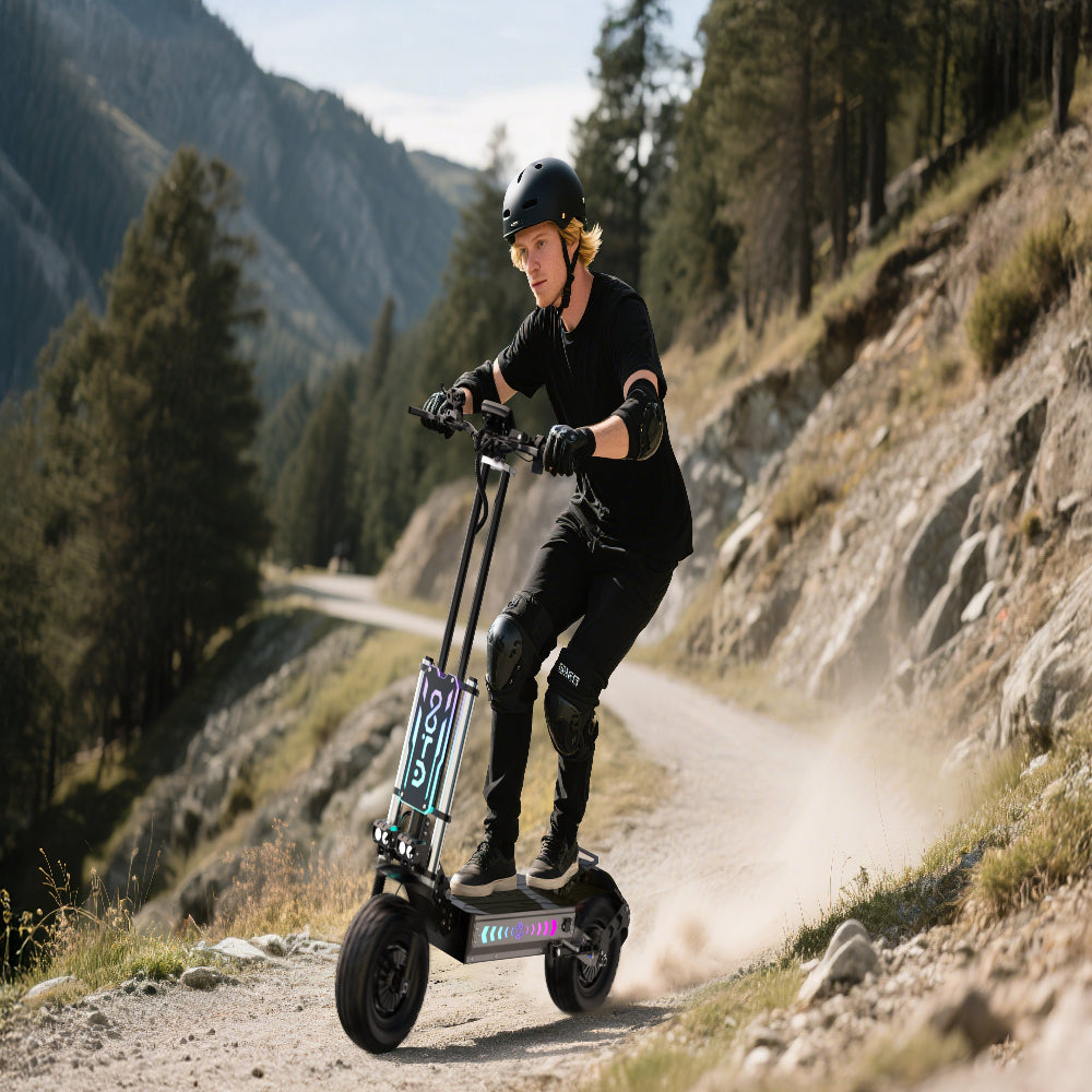 Persoon rijdt op een elektrische scooter op een bergpad met bomen en bergen op de achtergrond.