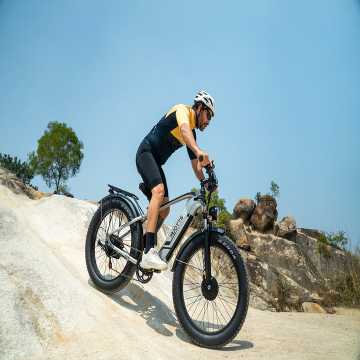 Person riding a mountain bike on a rocky trail with clear blue sky