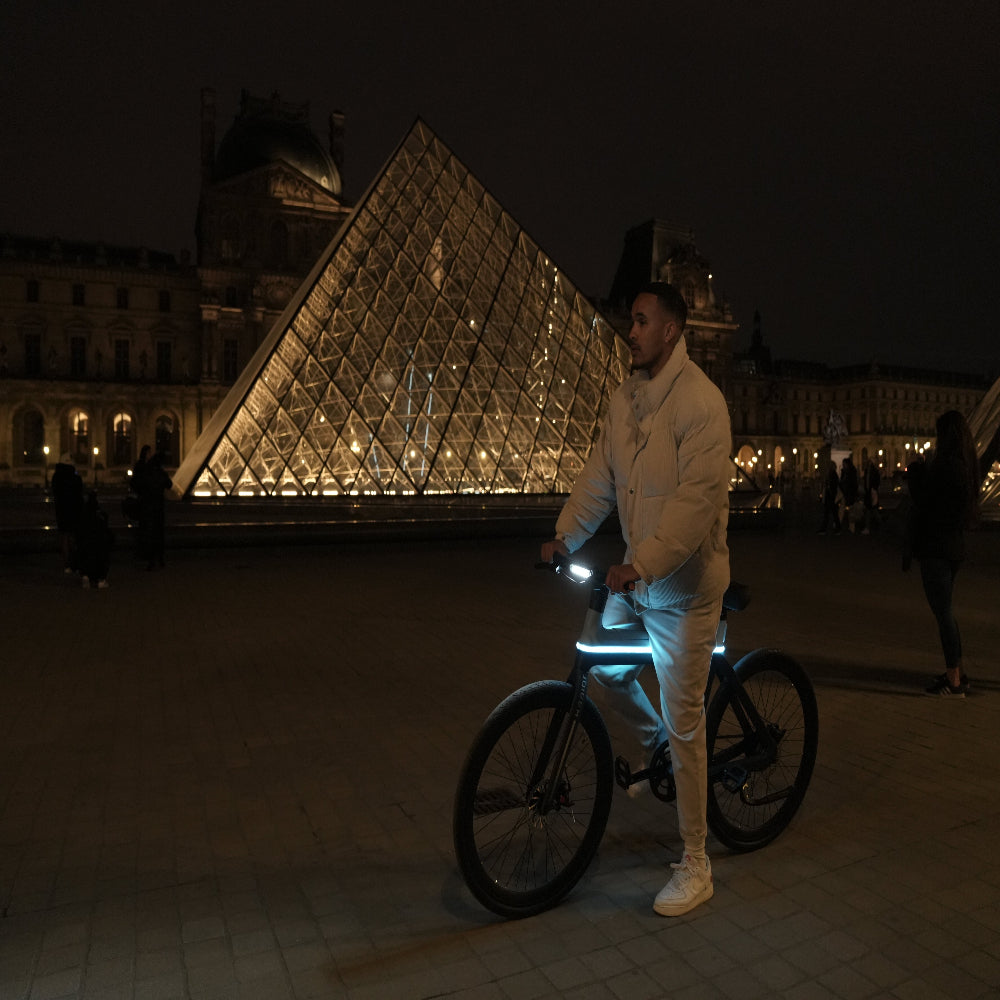 Person with a bicycle in front of the Louvre Pyramid at night