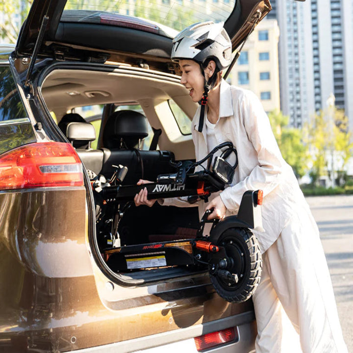 Person loading a scooter into the trunk of a car with a cityscape in the background