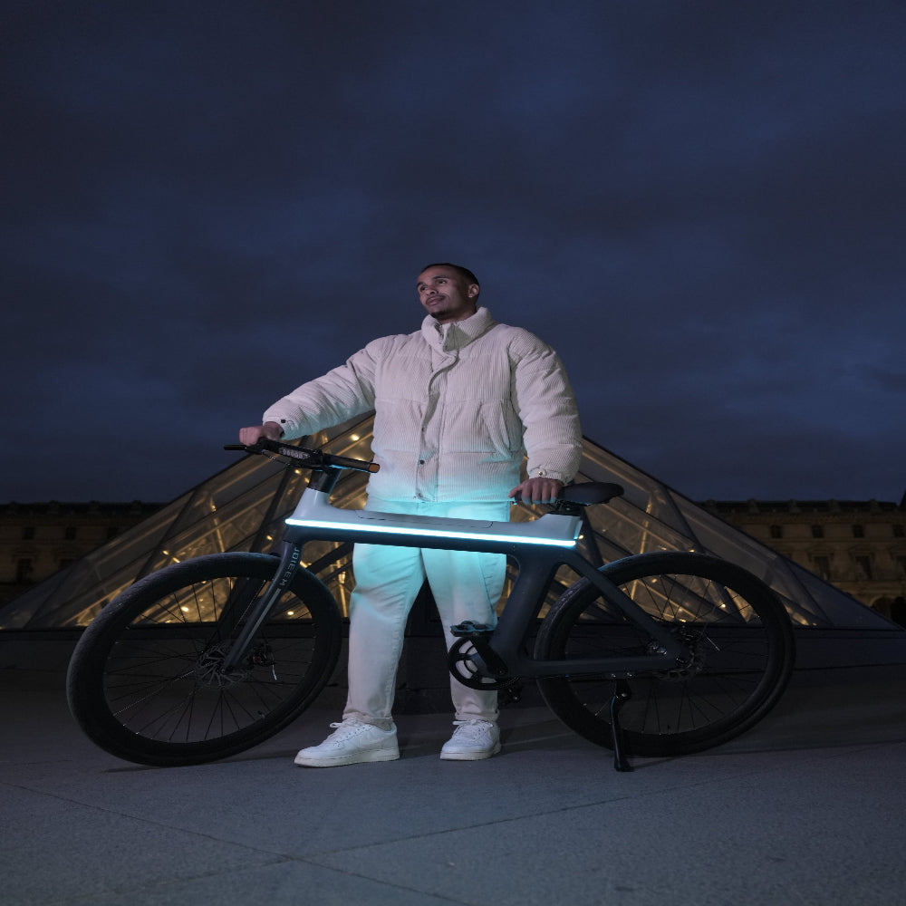 Person in a reflective suit standing next to a bicycle with a dark sky background