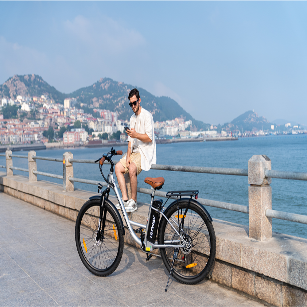 Man sitting on an electric bike by a waterfront with mountains in the background