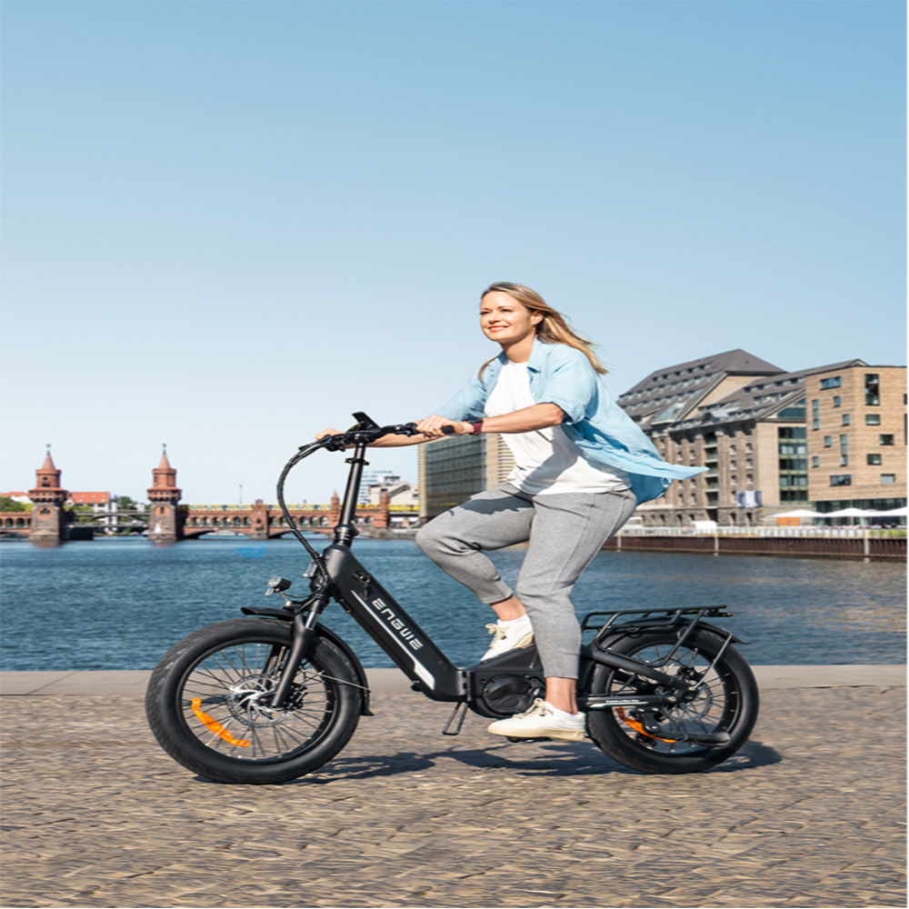Woman riding an electric bike by a waterfront with buildings in the background