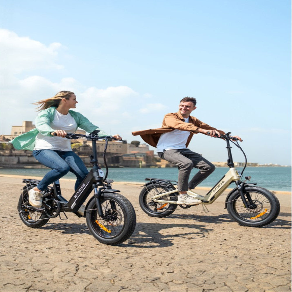 Two people riding electric bikes on a beach with a scenic background.