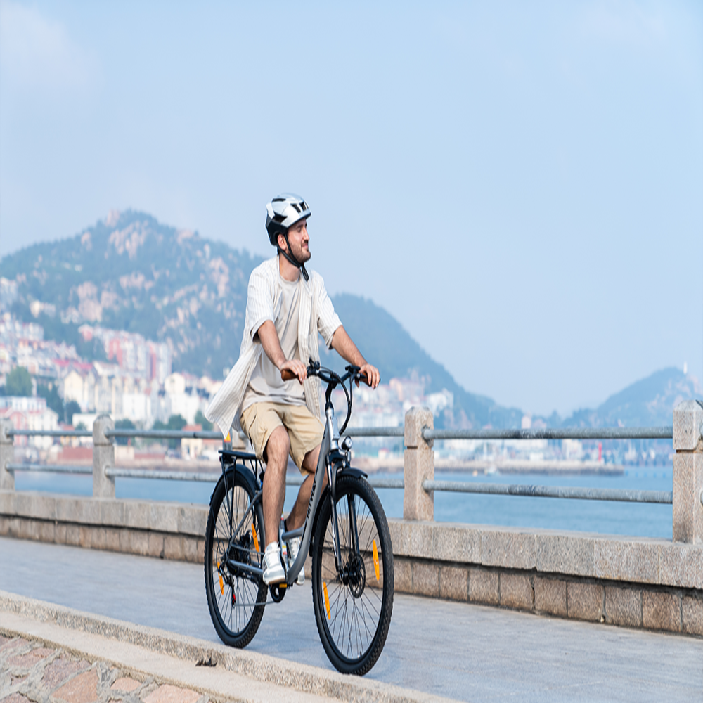 Man riding a bicycle on a scenic coastal path with mountains in the background
