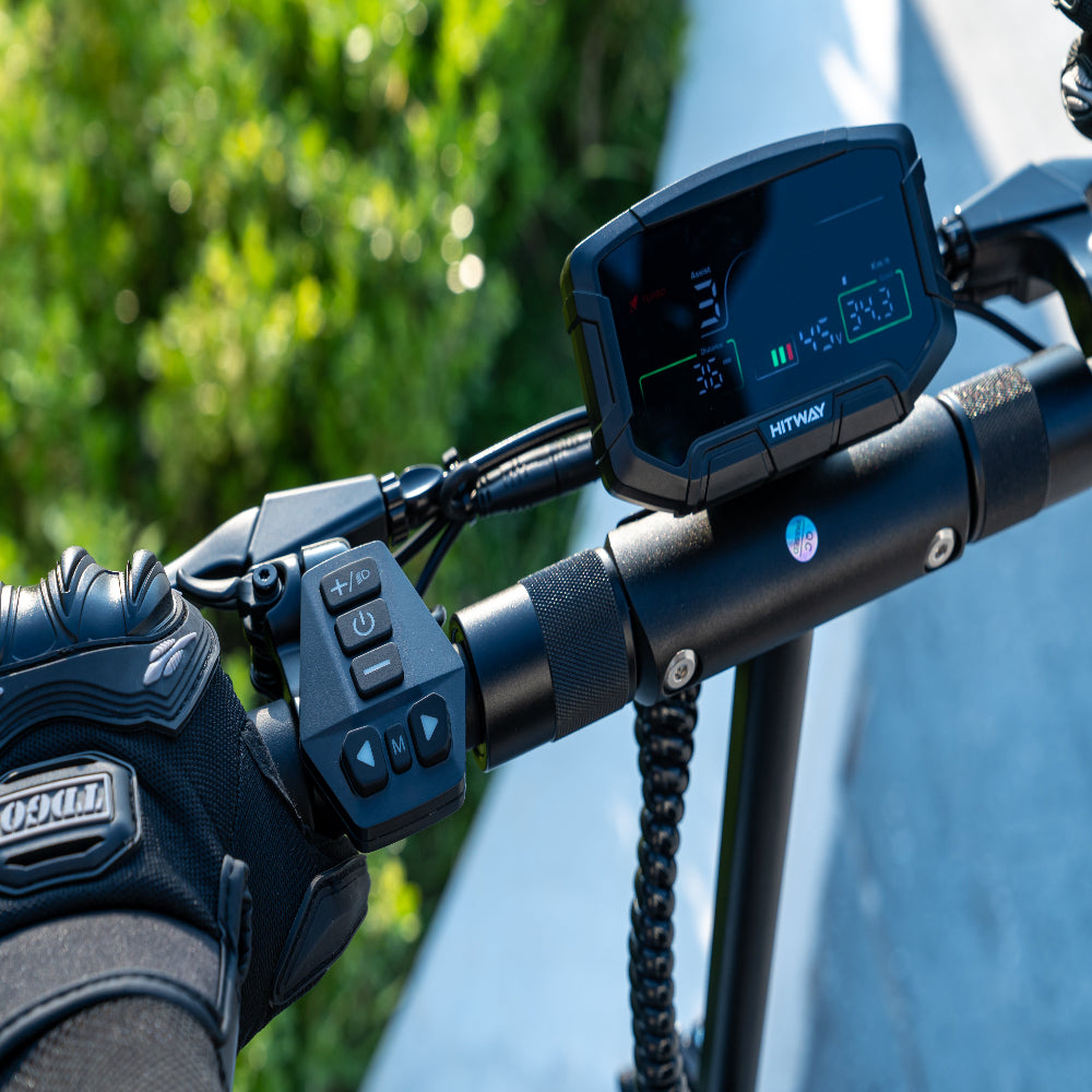 Close-up of a motorcycle handlebar with control panel and glove, blurred greenery in the background